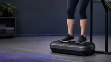 Ben i træningssko på en vibrationsplade ved et støttegelænder